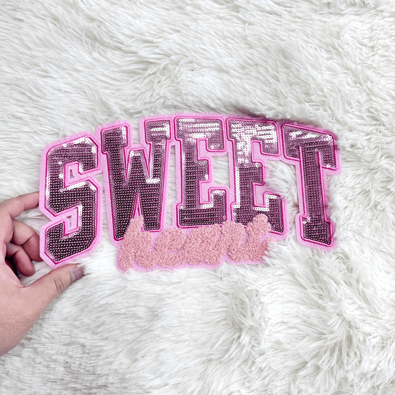 A sparkly pink "Sweetheart" patch laid out on a white fluffy rug.Patches