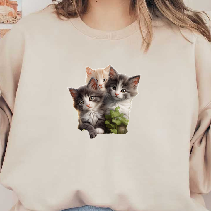 Tres adorables gatitos (uno atigrado gris, uno blanco y uno esponjoso de color crema) se acurrucan juntos con la vegetación detrás de ellos.