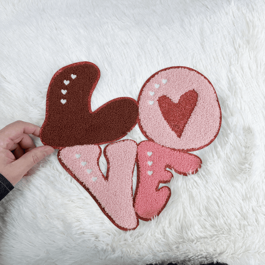 A charming plush "LOVE" decoration, featuring playful heart designs in pink and brown hues, perfect for adding warmth to any space.Patches