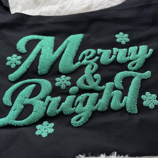 This festive black fabric features sparkly green lettering that reads "Merry & Bright," adorned with small snowflake designs.DTF Transfers puff