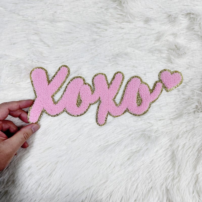 A playful pink "XOXO" sign with glittery gold accents, perfect for adding a touch of love to any space.Patches