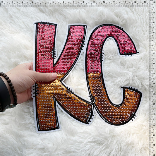 This vibrant, sequined "KC" letter decoration features a gradient of pink and gold tones, perfect for a stylish touch!Patches