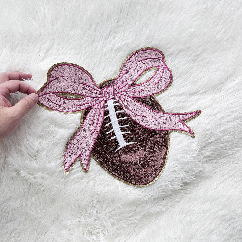 This charming pink and brown football patch, adorned with a sparkling ribbon, adds a playful touch to any outfit or accessory.Patches