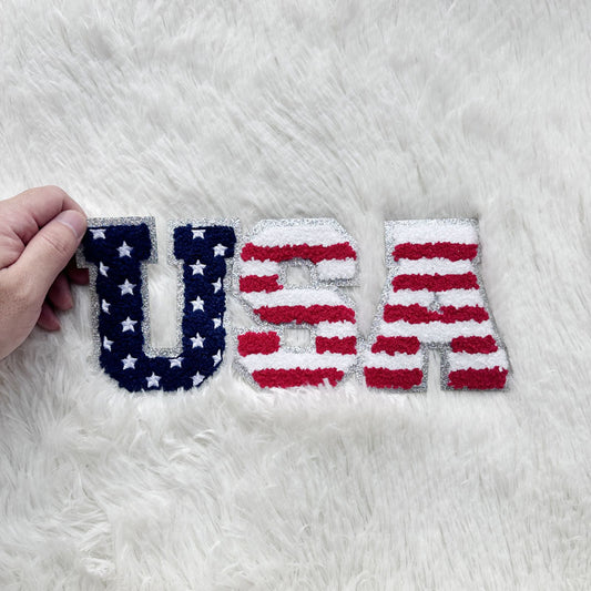 This decorative "USA" banner features a vibrant design with the stars and stripes of the American flag in plush material.Patches