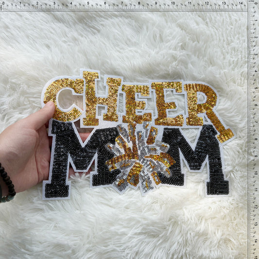 A sparkling "CHEER MOM" sign crafted from sequins in gold and black, perfect for showcasing support at cheer events.Patches