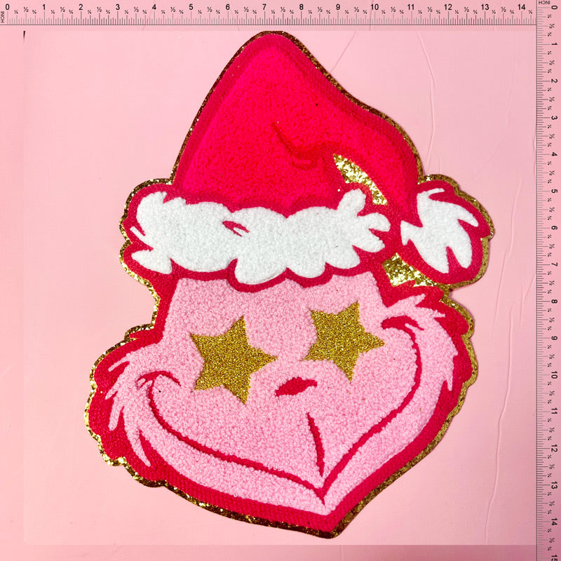 Bright and festive pink Grinch patch with a Santa hat, featuring glittery golden stars for a playful holiday touch.Patches