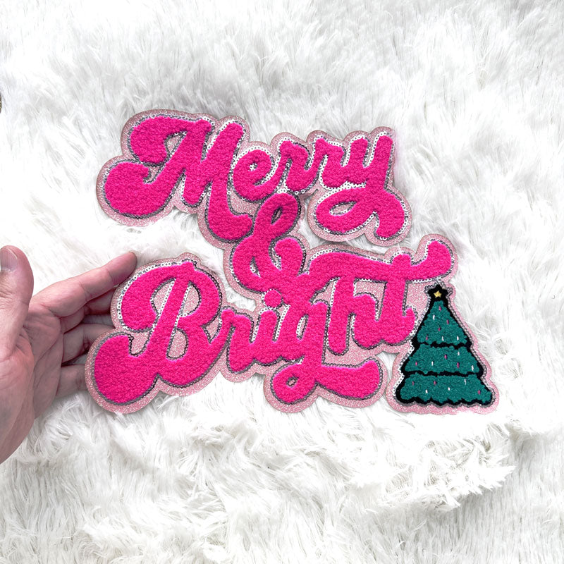 A vibrant pink felt decoration featuring the words "Merry & Bright" along with a playful green Christmas tree.Patches