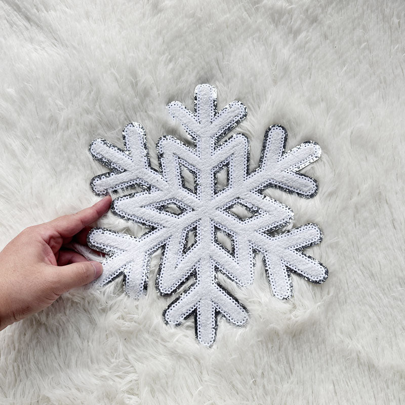 A decorative white snowflake shaped placemat adorned with sparkling sequins, perfect for winter-themed table settings or festive décor.Patches