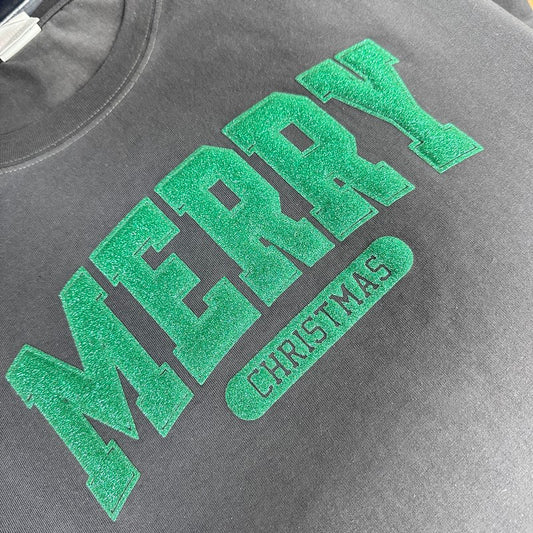 Celebrate the season with this cozy gray T-shirt featuring bold, glittery "MERRY CHRISTMAS" lettering in vibrant green.DTF Transfers puff