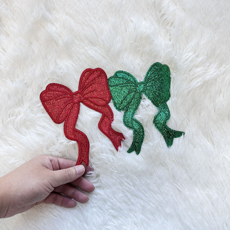 A festive Green/Red small glitter bow applique, perfect for adding a cheerful holiday touch to any garment or craft project.