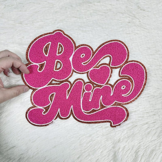 Vibrant pink chenille ‘Be Mine’ patch with gold glitter accents, perfect for adding charm to Valentine’s-themed crafts or outfits.