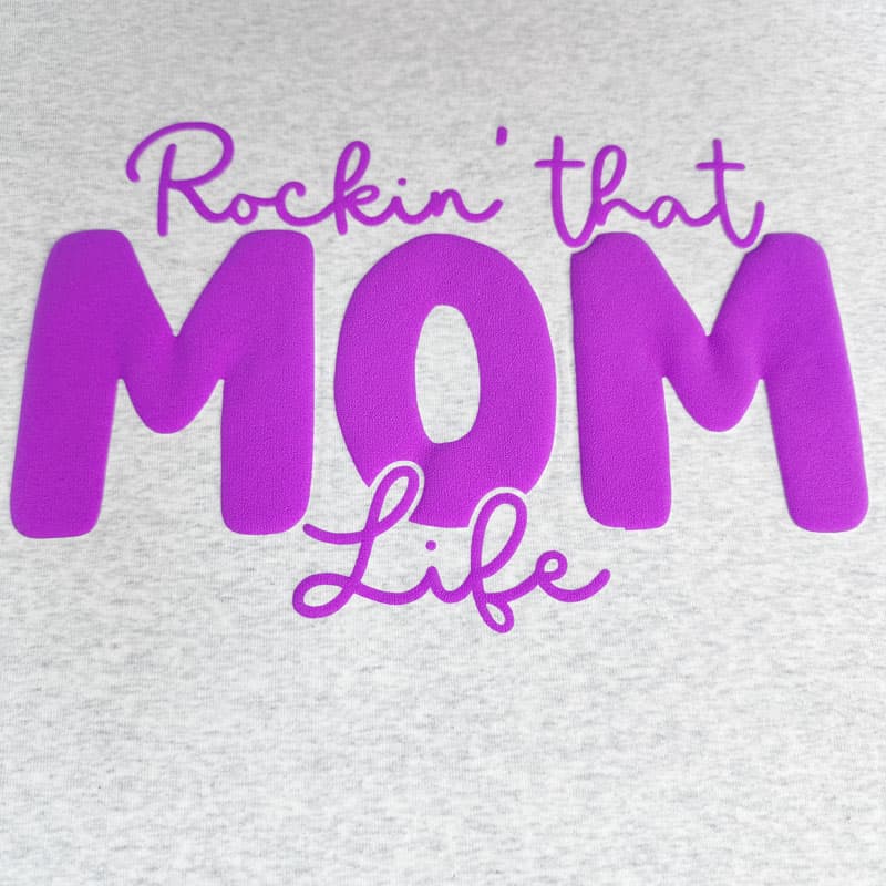 Embrace motherhood with this stylish black shirt featuring the playful phrase "Rockin' that MOM Life" in glittery pink lettering.DTF Transfers puff