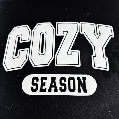 Stay warm and stylish this winter with this cozy black shirt featuring metallic silver lettering that reads "COZY SEASON."DTF Transfers puff