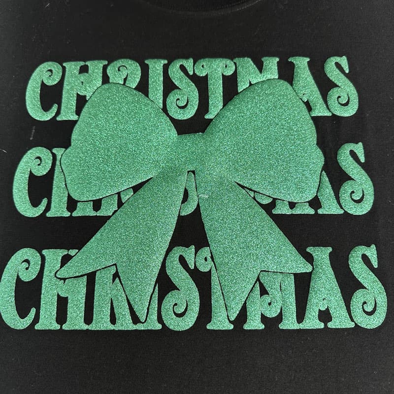 A festive green glitter bow with the word "CHRISTMAS" printed multiple times in a playful font. Perfect for holiday decorations!DTF Transfers puff