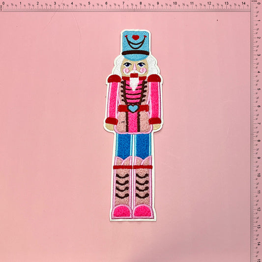 Colorful embroidered nutcracker decoration featuring a cheerful design with pink and blue accents, perfect for festive decor.Patches