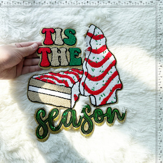 A festive, embroidered patch featuring the words "Tis the Season" alongside a whimsical dessert design in vibrant colors.Patches