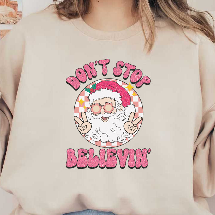 A cheerful Santa with glasses gives a peace sign, adorned with festive pink glitter text reading "DON'T STOP BELIEVIN'." heat press transfers