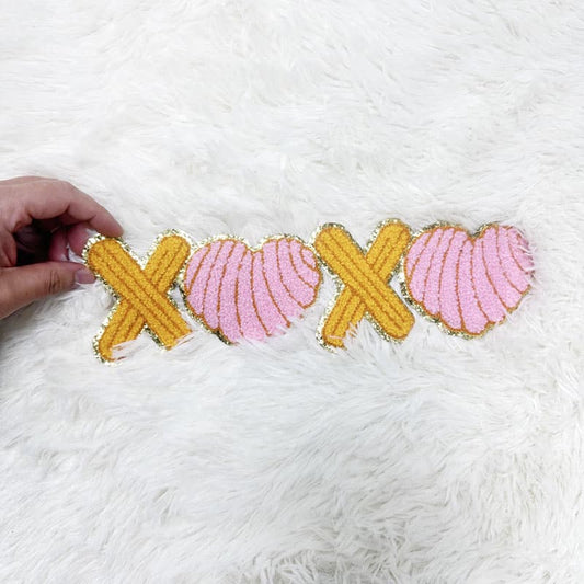 A colorful fabric patch featuring XOXO in pink and yellow, accented with golden edges for a playful touch.Patches