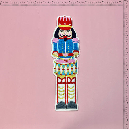 Colorful nutcracker design featuring intricate embroidery details, standing proudly atop a drum with vibrant reds, blues, and greens.Patches